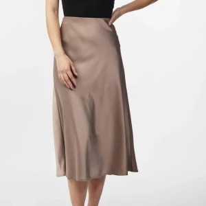 Beige satin kjol från Vero Moda - Säljer en elegant beige satin kjol från Vero Moda. Kjolen har en mjuk och glansig yta som ger en lyxig känsla. Den är i lång modell och passar perfekt för både vardag och fest. Kjolen är i storlek L och är helt ny med prislappen kvar.
