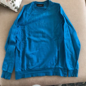 Blå tröja från Peak Performance - Säljer en snygg blå tröja från Peak Performance i storlek M. Tröjan är långärmad och har en normal passform. Den är gjord av bomull och har en broderad logga på bröstet. Perfekt för höst och vår! Tröjan är i fint skick!