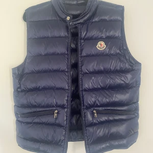 Moncler Gui Väst - Säljer de här västen då den är för liten. Västen är i väldigt bra skick knappt använd. Den är i stl 2 motsvarande s/m. Skriv vid frågor, mer bilder eller likande. Priset är ej hugget i sten.