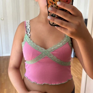 Rosa ribbad linnetopp från Sinsay - Säljer en superfin rosa ribbad linnetopp från Sinsay. Den har gröna spetsdetaljer och är croppad med smala axelband. Perfekt för sommaren. Toppen är i storlek M och i nyskick. 🌸