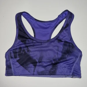 Lila sport-bh - Säljer en snygg lila sport-bh i syntetmaterial. Den har en cool, mörkare mönsterdetalj och är perfekt för träning. Den är ärmlös och har en tight passform för bästa stöd.
