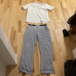 Pyjamas sett - Säljer ett par bekväma randiga byxor från Damella. De är blå och vita med en loose passform och knappar framtill. Perfekta för en avslappnad dag hemma eller sommarens lata dagar. Byxorna har en elastisk midja för extra komfort.