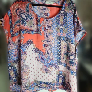 Mönstrad topp från Zizzi - Färgglad topp från Zizzi med ett unikt paisleymönster i cerise, blått och orange. Toppen har en lös passform och korta ärmar,  materialet känns lätt och luftigt. Har några år på nacken men inga defekter. 