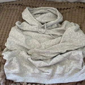 Grå hoodie från H&M - Mysig grå hoodie från H&M i storlek S. Perfekt för kyliga dagar med sin mjuka och bekväma passform. Den har en klassisk design med dragsko i huvan och en stor ficka framtill. Passar både för vardag och avslappnade stunder hemma.