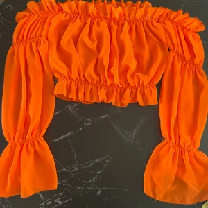 Orange offshoulder topp - Säljer en superfin orange offshoulder topp med långa ärmar. Den är croppad och har en elastisk kant vid axlar och midja för en bekväm passform. Perfekt för sommarens fester eller en dag på stan. 🧡
