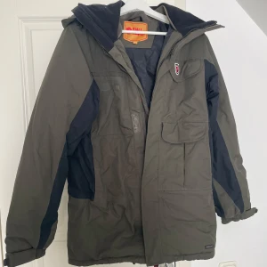 Fjällräven jacka  - En Fjällräven jacka i grönt med svarta detaljer. Jackan har en huva och flera fickor. Storlek XS.  Dam modell 