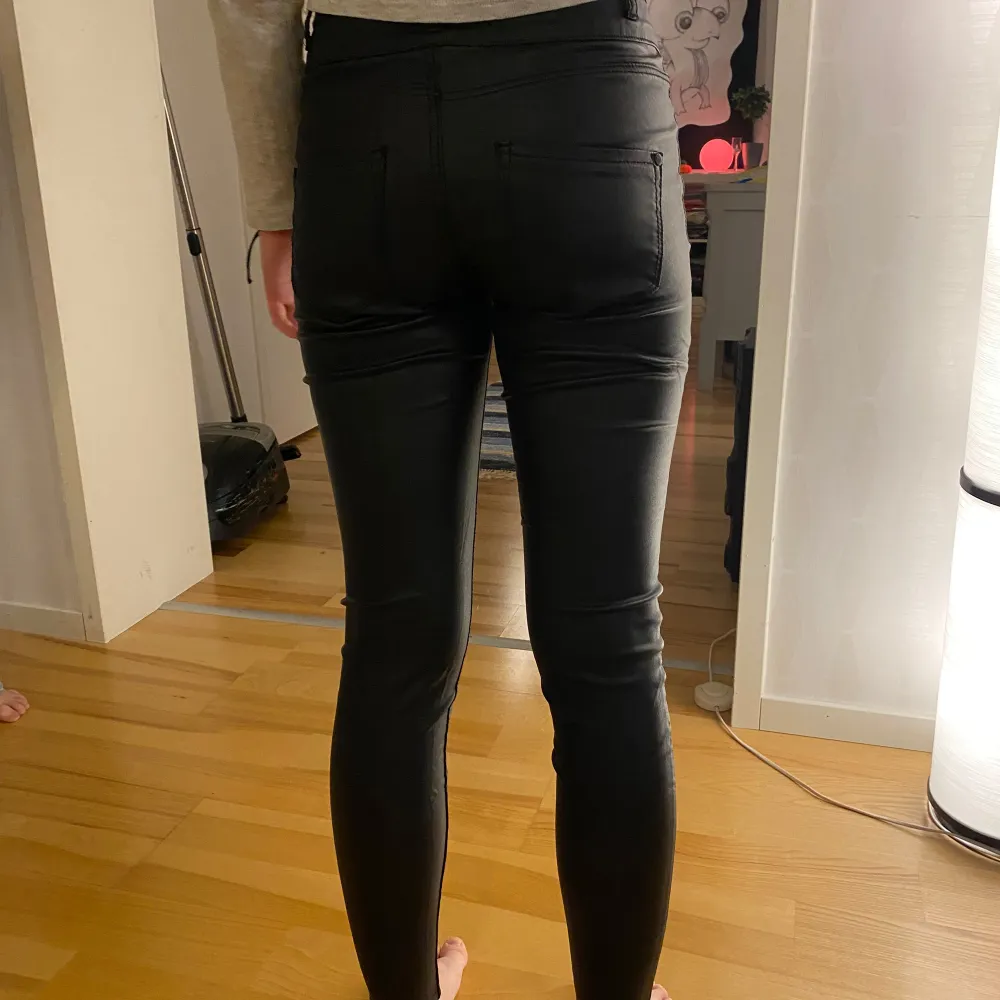 Säljer ett par svarta högmidjade skinny byxor i syntetmaterial. De har en snygg knapprad framtill och sitter tight för en smickrande passform. Perfekta för både vardag och fest! Det enda att anmärka är färgsläpp på knapparna. . Jeans & Byxor.