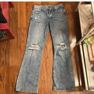 Blå jeans från Shein - Säljer ett par blå jeans från Shein i storlek XS. De har en cool distressed look med slitningar på knäna och en bootcut-stil. Perfekta för en avslappnad vardagsstil. De är i bra skick och redo för en ny ägare!