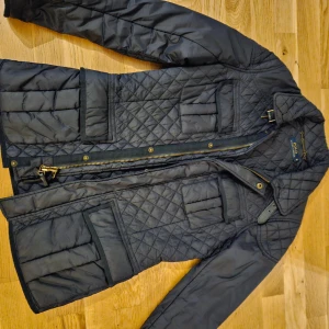 Svart quiltad jacka från Polo Ralph Lauren - Säljer en snygg svart quiltad jacka från Polo Ralph Lauren. Den har en dragkedja och knappar framtill, samt flera praktiska fickor. Perfekt för höst och vår med sin stilrena design och bekväma passform. Jackan är i mycket bra skick och redo för nya äventyr!