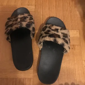 Leopardmönstrade sandaler med pälsdetalj - Säljer ett par coola sandaler med leopardmönstrad pälsdetalj. Perfekta för att liva upp vilken outfit som helst! De har en bekväm svart sula och är lätta att glida i. Perfekta för sommardagar eller som inneskor. Storlek 40. Kan mötas upp i Hbg eller skickas 