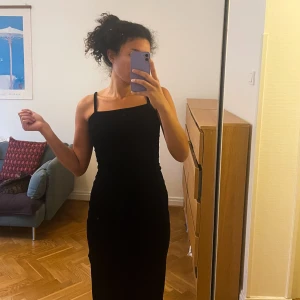 Svart klänning med mönster - Säljer en elegant svart klänning med smala axelband och ett subtilt mönster. Klänningen är tight och passar perfekt för festliga tillfällen. Materialet ser ut att vara mjukt och bekvämt, vilket gör den både stilren och skön att bära.