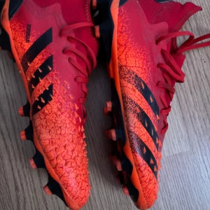 Röda fotbollsskor från Adidas - Säljer ett par coola röda fotbollsskor från Adidas. De har en grym design med svarta detaljer och snörning. Perfekta för fotbollsträningen eller matchen. Skorna har en robust sula med dobbar för bra grepp på planen. Använda men i bra skick!