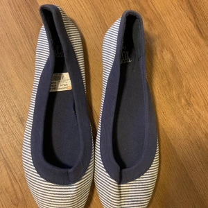 Randiga ballerinaskor från Vox - Säljer ett par snygga randiga ballerinaskor från Vox i blått och vitt. De har en klassisk design med rund tå och är perfekta för vår och sommar. Skorna är i mycket bra skick och har en bekväm passform. Perfekta för både vardag och fest!