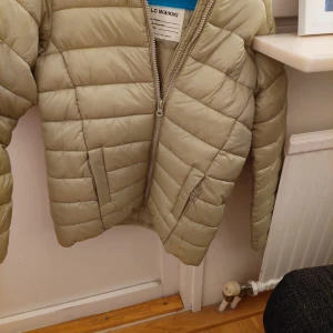 Beige pufferjacka från LC Waikiki - Säljer en snygg beige pufferjacka från LC Waikiki. Jackan har en dragkedja framtill och är perfekt för kyliga dagar. Den är i bra skick och passar barn i åldern 10-11 år. Perfekt för höst och vinter!