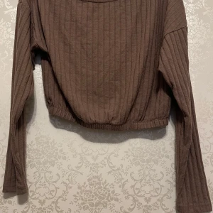 Brun ribbad tröja - Säljer en snygg brun ribbad tröja med långa ärmar. Perfekt för höst och vinter, den är både stilren och bekväm. Tröjan har en croppad passform som ger en modern look. Perfekt för att matcha med jeans eller kjol!