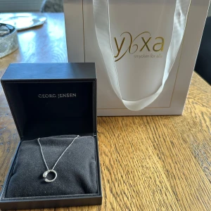 Silverhalsband från Georg Jensen - Säljer ett elegant silverhalsband från Georg Jensen. Halsbandet tillhör kollektionen Mercy (litet). Det har en enkel och stilren design med ett cirkelformat hängsmycke. Perfekt för både vardag och fest. Kommer i originalförpackning.