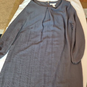 Grå klänning från H&M - Säljer en snygg grå klänning från H&M i storlek L. Klänningen har en enkel och stilren design med långärmade ärmar och en dragkedja i ryggen. Perfekt för både vardag och fest! 💖