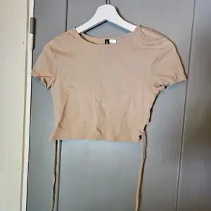 Säljer en beige croppad topp från H&M Divided. Toppen är kortärmad och har en tight passform. lite kortare i bak för att man ska knyta snörena för en fin detalj. knappt använd