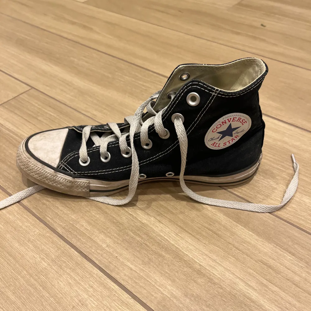 Säljer ett par svarta Converse All Star sneakers i storlek 39. Skorna är välanvända med vita snören och en vit sula som har blivit lite smutsig. De har den klassiska höga modellen med snörning och Converse-loggan på sidan. Perfekta för en casual look!. Skor.