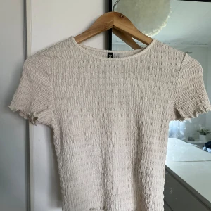 Beige ribbad topp - Säljer en superfin vitcremefärgad ribbad topp i storlek XS passar även S då den är väldigt stretchig. Den är kortärmad och har en tight passform som framhäver figuren. Perfekt för både vardag och fest! Toppen är i nyskick och väldigt bekväm att ha på sig.