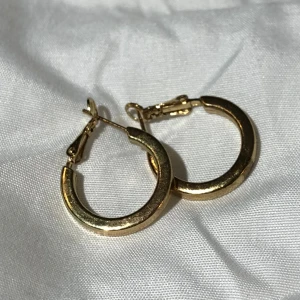 Örhöngen - Guldfärgade örhängen. Finns en defekt på ena örhänget, syns på bild två. Storlek ca 2cm. Vikt ca 2g.