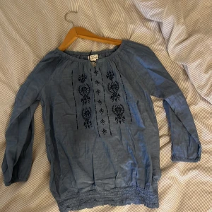 Blå blus med broderi - Säljer en söt blå blus med broderi på framsidan. Blusen har långa ärmar och en elastisk nederkant som ger en fin passform. Perfekt för både vardag och fest!