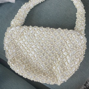 Vit handväska med pärlor - Säljer en superfin vit handväska som är täckt med pärlor. Väskan har en unik och elegant design som passar perfekt för festliga tillfällen. Den är i nyskick och har en bekväm axelrem som också är dekorerad med pärlor. Perfekt för att ge din outfit en extra touch av glamour!