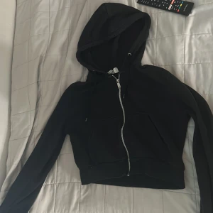 Svart hoodie med dragkedja - Säljer en svart hoodie med dragkedja framtill. Den har en stor huva och är långärmad. Perfekt för höst och vinter. Den är i bra skick och väldigt bekväm att ha på sig. Passar till både vardag och träning. ganska liten i storleken och lite kortare
