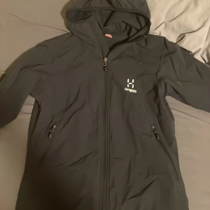 Haglöfs jacka - Säljer en svart jacka från Haglöfs med huva och dragkedja. Jackan har två fickor med dragkedjor och är perfekt för utomhusaktiviteter. Den är designad för kvinnor och har en stilren look. har andvänts 3 gånger har inte kvito dock tyvär