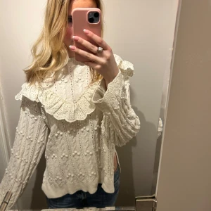 Vit blus med spetsdetaljer - Säljer en romantisk vit blus med spetsdetaljer och volang runt halsen. Blusen har långa ärmar och ett vackert broderat mönster. Perfekt för en stilfull look.