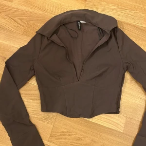Brun croppad topp från Divided - Säljer en brun croppad topp från Divided med långa ärmar och en djup krage. Toppen är i ett mjukt material som känns skönt mot huden.