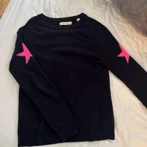 Mörkblå tröja med rosa stjärnor - Säljer en svart tröja från Chinti & Parker med coola rosa stjärnor på ärmarna. Tröjan har en normal passform och är perfekt för både höst och vinter. Den är långärmad i ett Kashmirblandat tyg som är jättegosigt. 🌟