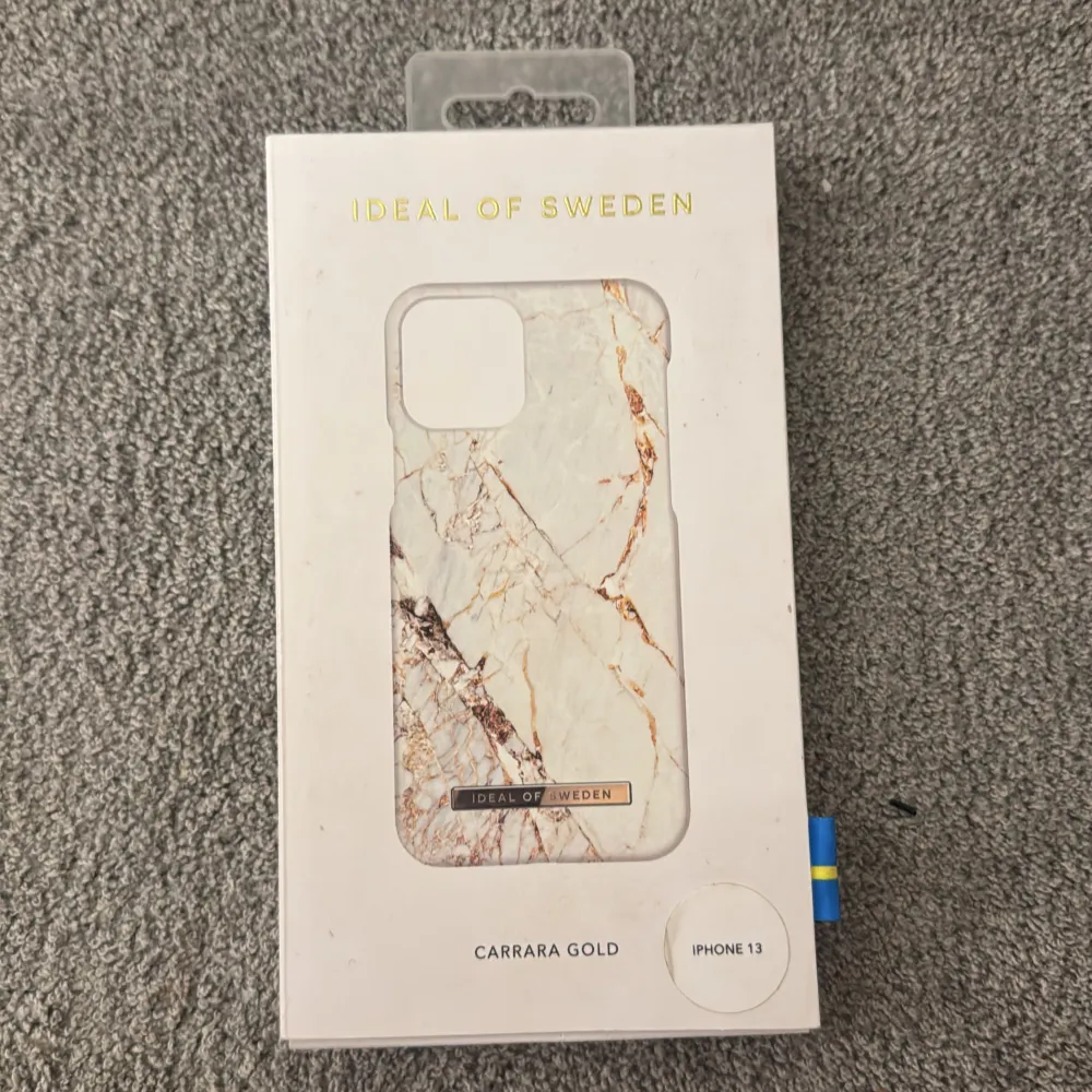 Snyggt mobilskal i Carrara Gold design från IDEAL OF SWEDEN, anpassat för iPhone 13. Skalet har ett elegant marmormönster i vitt och guld som ger en lyxig känsla. Perfekt för att skydda din telefon med stil. Aldrig använt för att jag beställde fel storlek, köpte för 400kr💕. Asusteet.