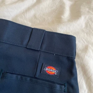 Mörkblå byxor från Dickies - Snygga mörkblå byxor från Dickies, modell 874 Original Fit. De har en klassisk design med hällor för bälte och en stilren look. Perfekta för en avslappnad men ändå stilren stil.