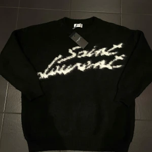 Svart tröja från Saint Laurent - Tjock varm stickad tröja från Saint Laurent med vit text på framsidan. Ny med lappar. Bredd ca 65 cm längd 71 cm. Vid frågor är det bara att skriva:)