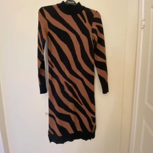 Zebramönstrad klänning från Vila Stl XS - Snygg zebramönstrad klänning från Vila i svart och brun. Klänningen har en tight passform och är långärmad. Slitsar på båda sidor.  Använd ett fåtal gånger. 