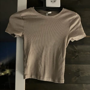 Beige ribbad topp - Säljer en stilren beige ribbad topp med korta ärmar. Perfekt för en avslappnad look. Toppen har en rund halsringning och är gjord i ett mjukt material.