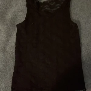 Svart spetslinne - Säljer ett snyggt svart spetslinne med ärmlös design. Perfekt för en stilren look med en touch av elegans. Linnet är figurnära och passar bra till både jeans och kjol.