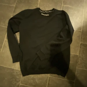 Svart tröja från Palm Angels - Säljer en svart tröja från Palm Angels med deras ikoniska logga i vitt på baksidan och vid halsen. Tröjan har långa ärmar och en klassisk passform. Perfekt för en stilren look.
