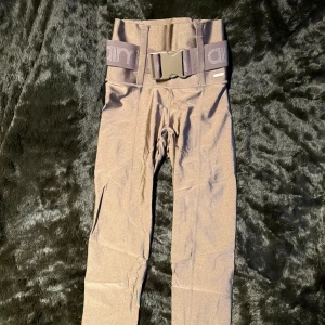 Aim’n träningsbyxor med bälte - Snygga beige träningsbyxor med ett brett elastiskt bälte och spänne. Byxorna har en tight passform och är perfekta för träning. Materialet verkar vara syntetiskt och ger en bekväm känsla.