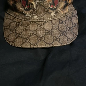 Mönstrad keps från Gucci - Snygg keps från Gucci med ikoniskt mönster och djurmotiv. Kepsen har en justerbar rem baktill med röd och grön rand. Perfekt för att ge din outfit en lyxig touch.