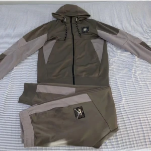 Grå hoodie och byxor från Nike Air Max - Säljer en grå hoodie och matchande byxor från Nike Air Max. Hoodien har dragkedja och justerbar huva med snören. Byxorna har elastisk midja och båda plaggen har Air Max-logga. Perfekt för en sportig look.