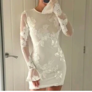 Vit blommig klänning - Elegant vit klänning med blommigt mönster och långa ärmar. Klänningen har en tight passform och är dekorerad med vackra spetsdetaljer. Perfekt för studenten