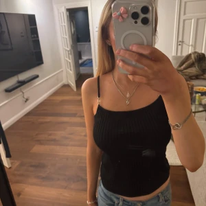 Svart ribbad linnetopp - Snygg svart ribbad linnetopp med smala axelband och en figurnära passform. Perfekt för en stilren look, lätt att matcha med jeans eller kjol. Smutset är på spegeln och inte på linnet💓💓