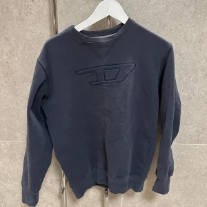 Mörkblå tröja från Diesel - Säljer en snygg mörkblå tröja från Diesel med ett diskret broderat märke på bröstet. Tröjan är tillverkad i en mjuk bomullsblandning och har långa ärmar samt ribbade muddar vid ärmslut och nederkant. Perfekt för en avslappnad stil. Säljes då jag växt ur denna, men otroligt fet disel tröja som gör sig bra till vilken outfit som helst!