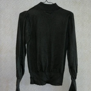 Svart polotröja från KappAhl - Säljer en stilren svart polotröja från KappAhl. Tröjan har långa ärmar och en ribbad polokrage som ger en klassisk look. Perfekt för kyligare dagar och lätt att matcha med olika outfits.