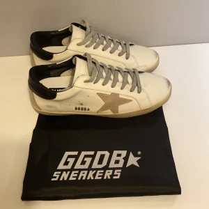 Vita golden goose sneakers  - Snygga vita sneakers från GGDB med en ikonisk stjärndetalj i beige på sidan💫. Skorna har grå snörning och en svart häl. Perfekta inför sommaren☀️. Dustbag följer med‼️ låda följer inte med de är därför priset är lite lägre‼️Fråga om ni undrar något priset är ej hugget i sten‼️De svart märkena är design skorna är i skick 9.9/10💯