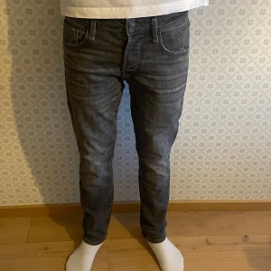 Grå jeansbyxor från Jack and jones - Snygga grå jeans från Jack and jones med en slim passform och klassisk femficksdesign. Byxorna har en dragkedja och knapp framtill. Perfekta för en stilren look. Storlek W28 L30 och modell Slim Straight/Tim. Om du har någon fundering är det bara att höra av sig. Mvh Levi!