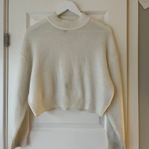 Vit stickad tröja från H&M - Säljer en vit stickad tröja från H&M med en croppad design och långa ärmar. Tröjan har en ribbad krage och är perfekt för en stilren look. Har en ljus fläck i mitten av tröjan💗