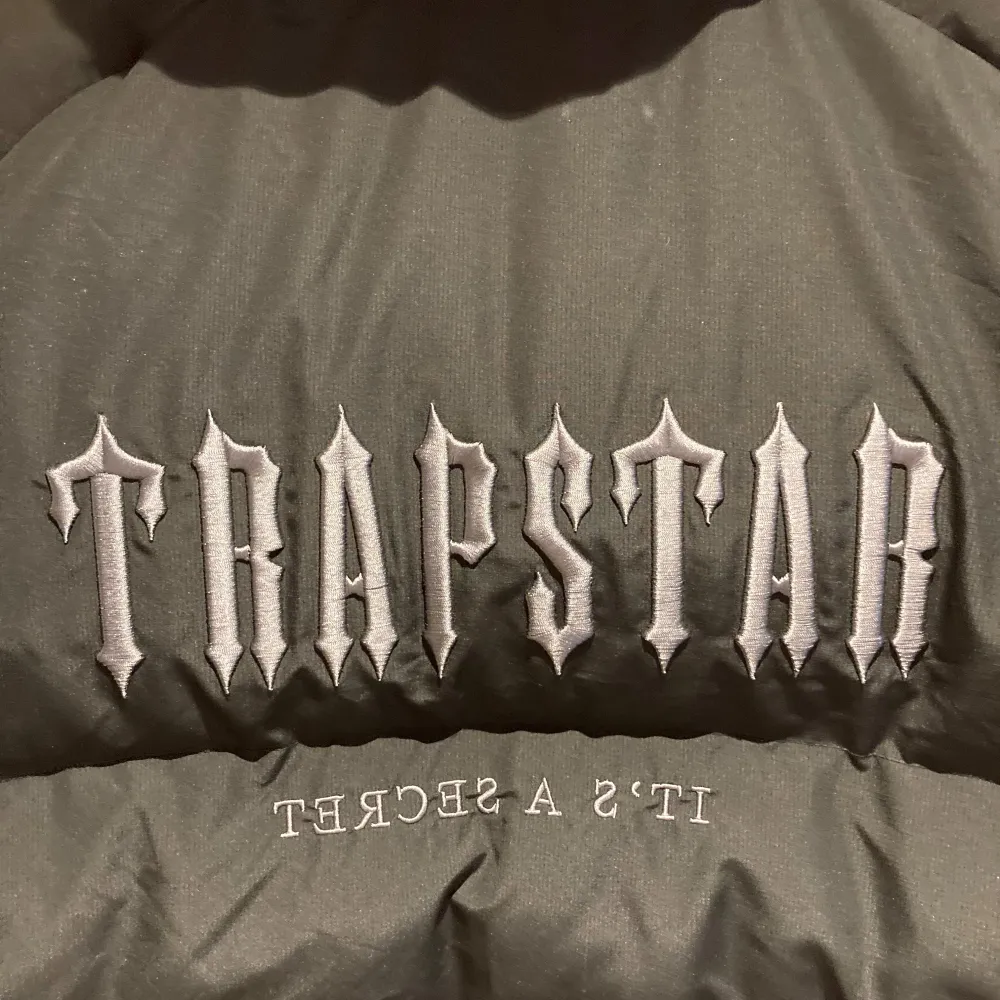 Säljer en svart pufferjacka från Trapstar med broderad text. Jackan är perfekt för vintern. Jackan är i nyskick och aldrig använd. Säljer då den är för stor.. Jackor.